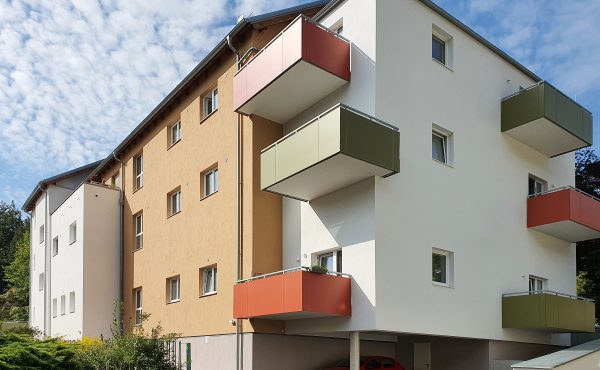 Moderner Wohnblock mit bunten Balkonen und geparktem Auto bei Sonnenschein.
