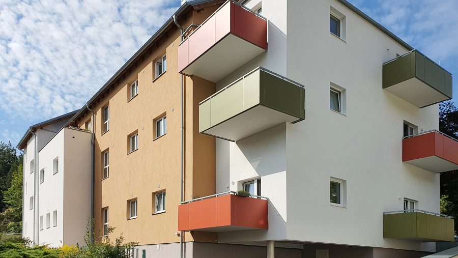 Moderner Wohnblock mit bunten Balkonen und geparktem Auto bei Sonnenschein.